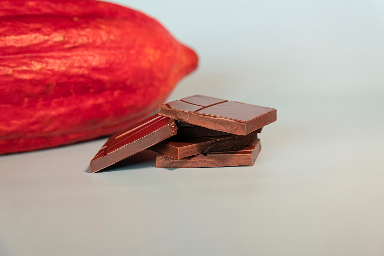 Chocolate bars with a cacao pod in the background on a light surface