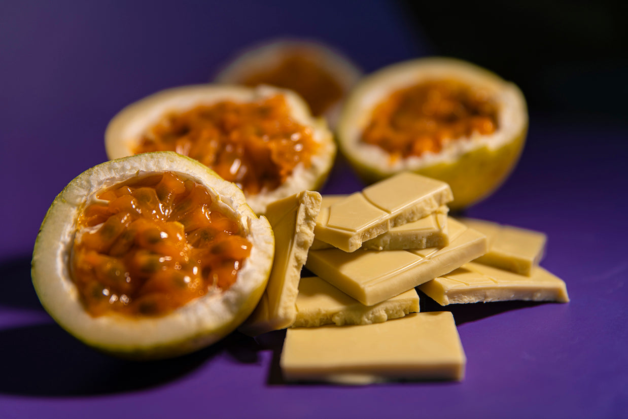 Halved passion fruits with white chocolate pieces on a purple background