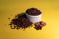 A small white ramekin overflowing with cocoa nibs on a yellow background