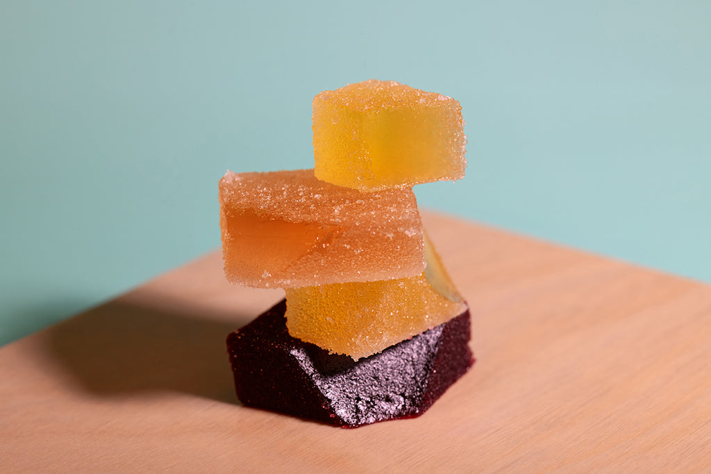 Stack of colorful pate de fruit (Orchard Gems) on a wooden surface with a light blue background