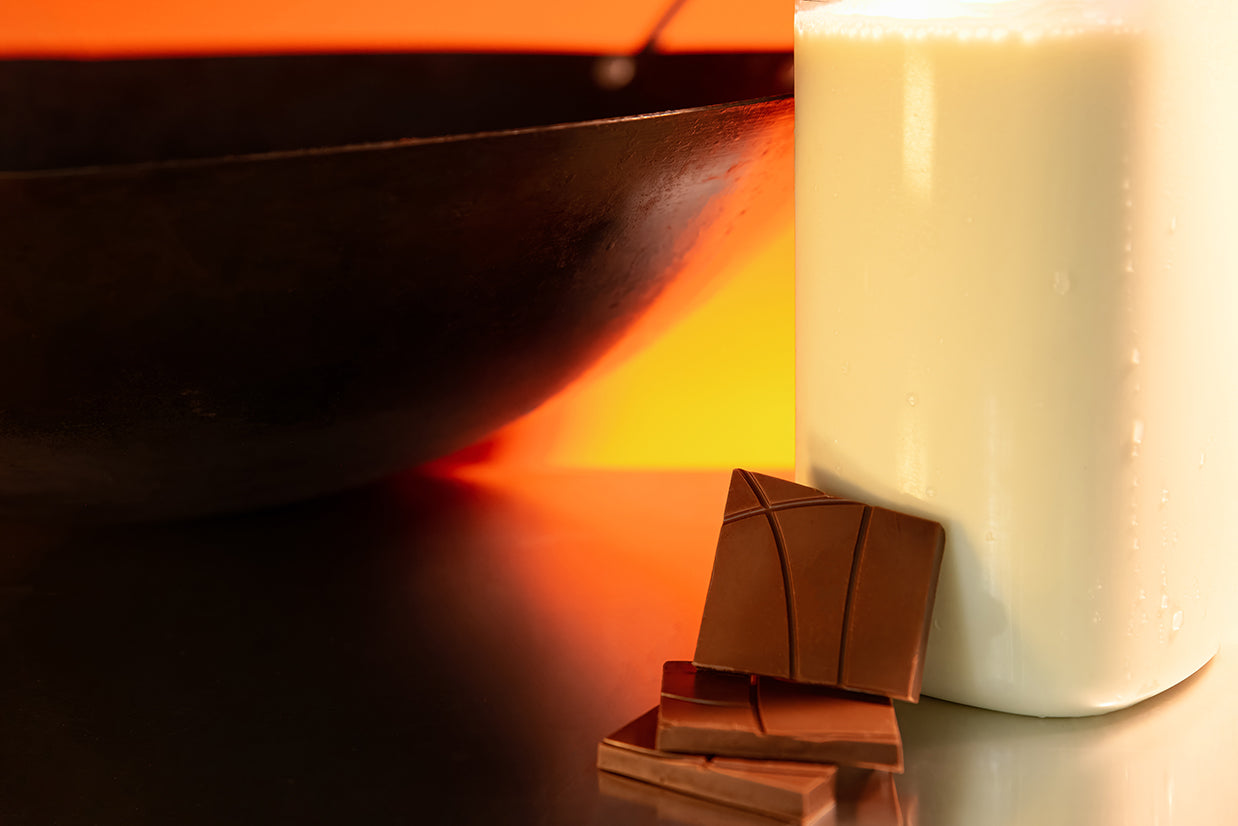 Chocolate bars and a glass milk jar on a reflective surface with a wok in a warm color tone