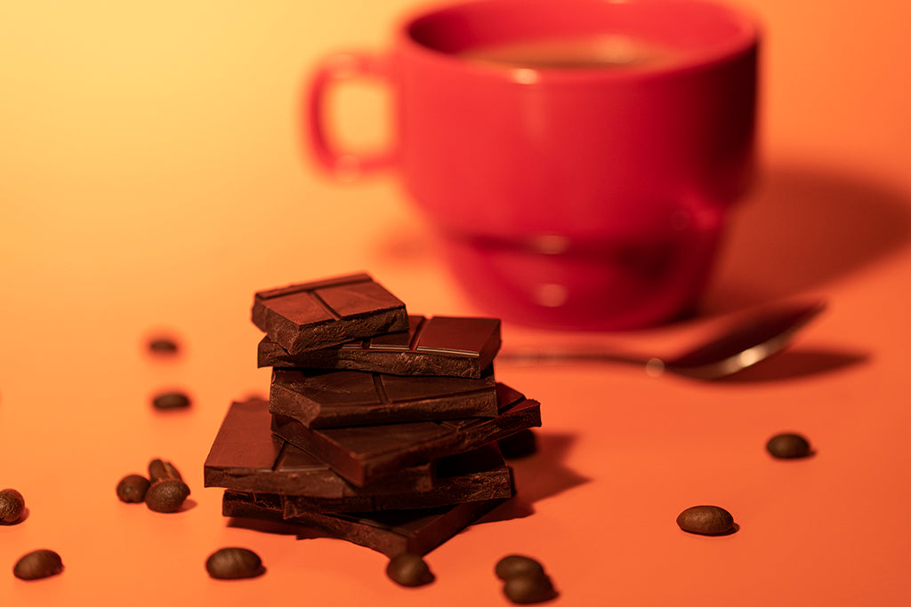 Stack of dark chocolate bars with a red mug and spoon on a warm-toned background
