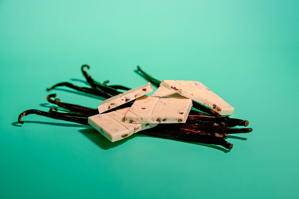 Vanilla beans with Mauna Kea Snow bar pieces on them atop a green background